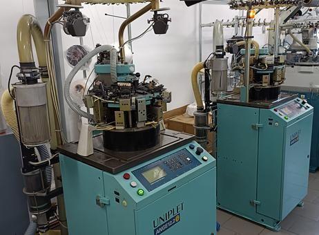 Two industrial knitting machines with control panels in a textile factory setting.